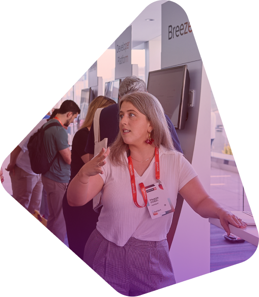 Woman with red lanyard presenting at conference booth with attendees in background