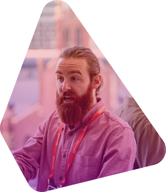 Bearded man in button-up shirt with red lanyard speaking at conference event