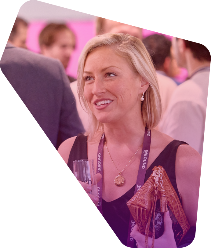 Smiling blonde woman in dark top at conference event, wearing lanyard and holding drink