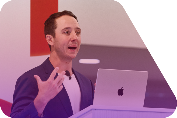 Man in dark jacket presenting at conference with laptop, gesturing while speaking